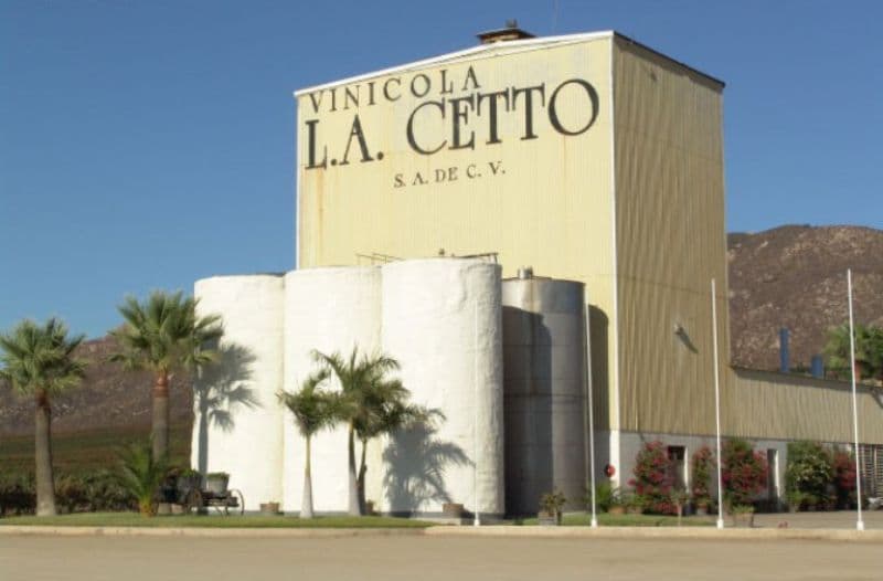 L.A. Cetto winery building with its name on the facade, wine tanks, and palm trees.