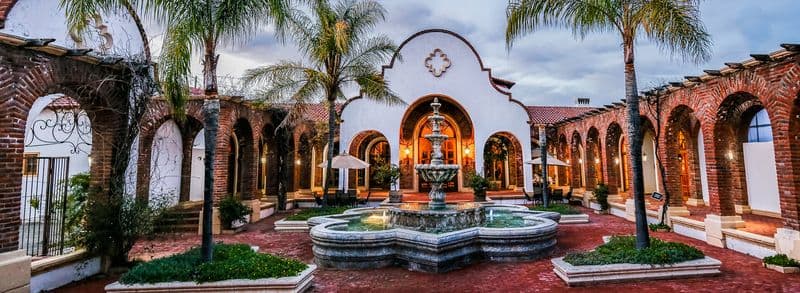 Adobe Guadalupe courtyard with a central fountain, brick arches, and palm trees.