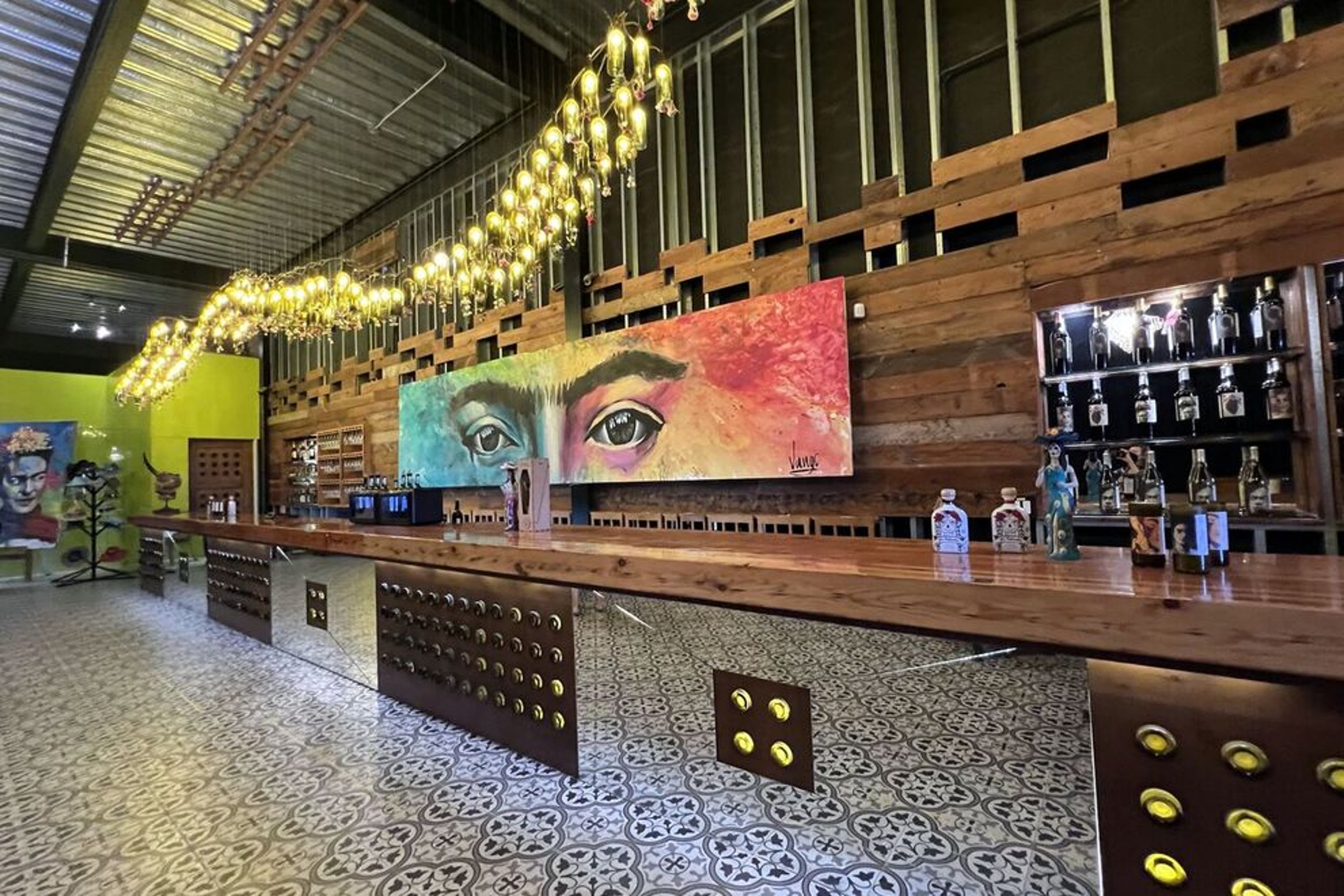 Wine bar at Casa Frida with a colorful mural, hanging lights, and patterned tiles.