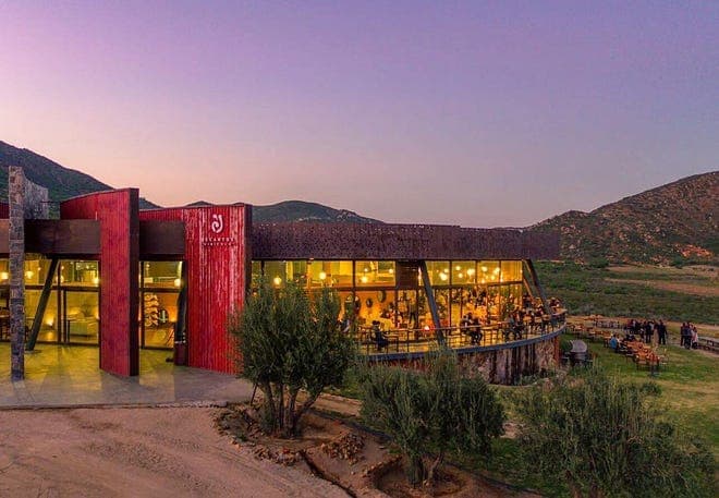 Decantos Vinícola’s glass-fronted winery and terrace against the hills at dusk.