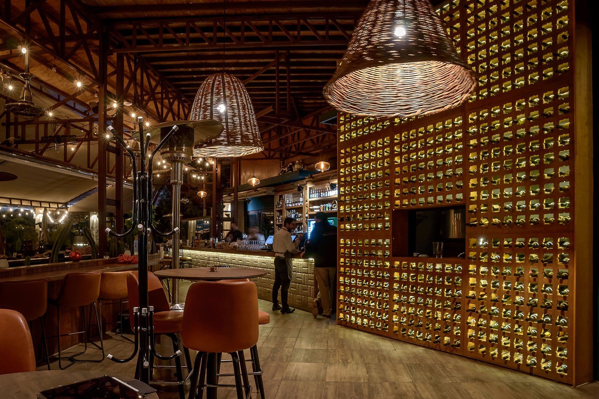 Fuego Cocina del Valle’s warmly lit bar with woven pendant lamps and a wall of wine bottles.